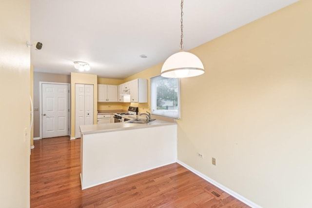 kitchen with sink, white cabinetry, light hardwood / wood-style floors, range with gas cooktop, and kitchen peninsula