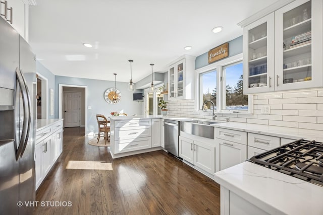 kitchen with dark wood-style floors, a peninsula, light stone countertops, stainless steel appliances, and a sink