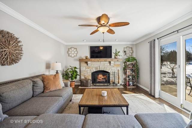 living area featuring a fireplace, crown molding, a ceiling fan, wood finished floors, and baseboards