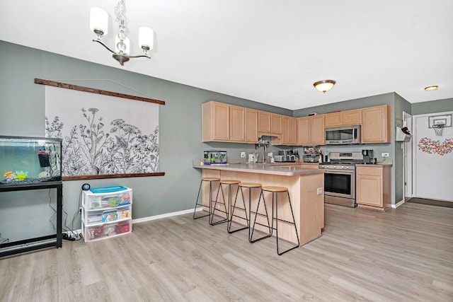 kitchen with light brown cabinetry, a breakfast bar, light hardwood / wood-style flooring, appliances with stainless steel finishes, and pendant lighting