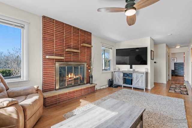 living room featuring a fireplace, light hardwood / wood-style flooring, a baseboard radiator, and ceiling fan