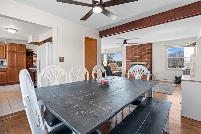 dining space featuring baseboard heating, a fireplace, beamed ceiling, and light wood-type flooring