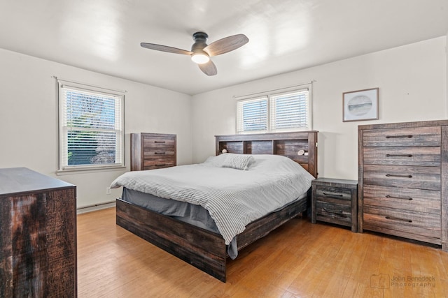 bedroom featuring multiple windows, light hardwood / wood-style flooring, ceiling fan, and baseboard heating