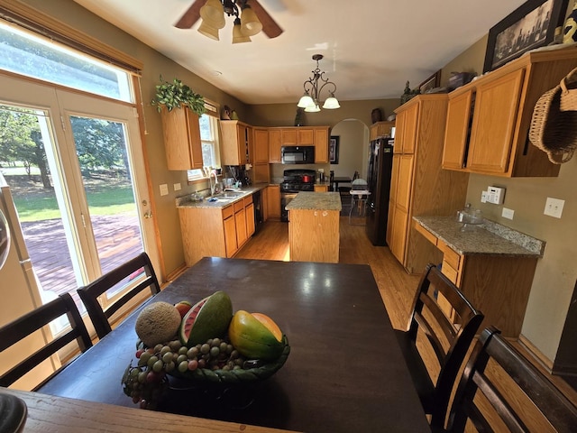 kitchen with pendant lighting, sink, light hardwood / wood-style flooring, a center island, and black appliances