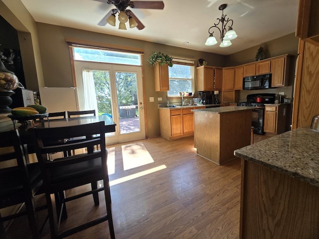 kitchen featuring decorative light fixtures, a kitchen island, light stone countertops, hardwood / wood-style floors, and black appliances