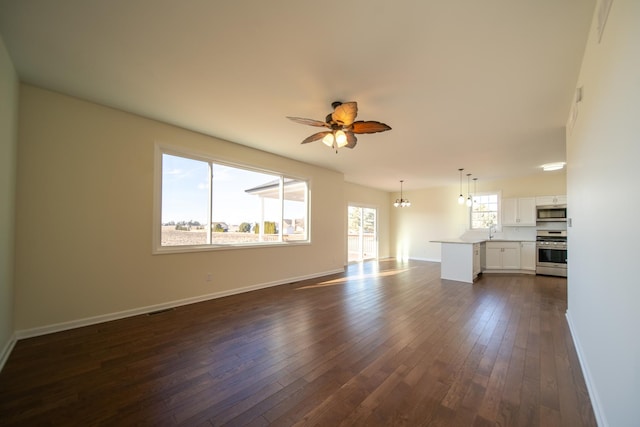 unfurnished living room featuring sink, dark hardwood / wood-style flooring, and ceiling fan with notable chandelier