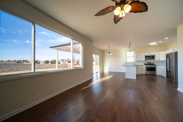 unfurnished living room with sink, dark hardwood / wood-style floors, ceiling fan with notable chandelier, and a wealth of natural light