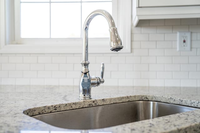 room details featuring light stone counters, sink, and decorative backsplash