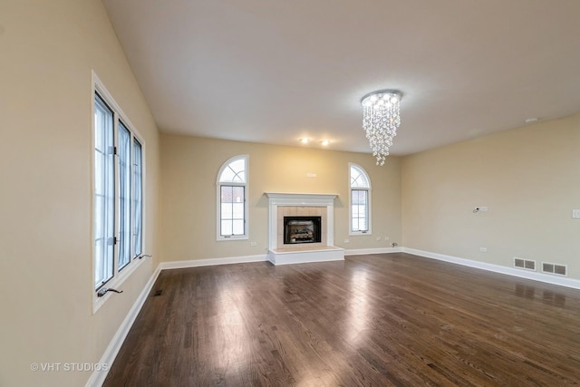 unfurnished living room featuring a tile fireplace, a healthy amount of sunlight, dark wood-type flooring, and a notable chandelier