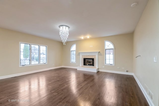 unfurnished living room featuring dark hardwood / wood-style flooring, a tiled fireplace, a wealth of natural light, and an inviting chandelier