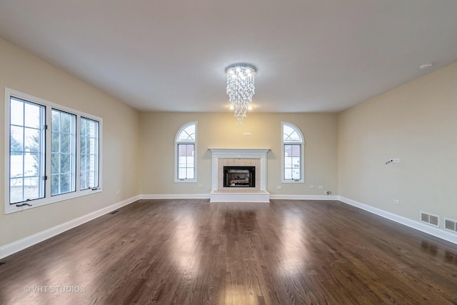 unfurnished living room with plenty of natural light, dark wood-type flooring, an inviting chandelier, and a fireplace