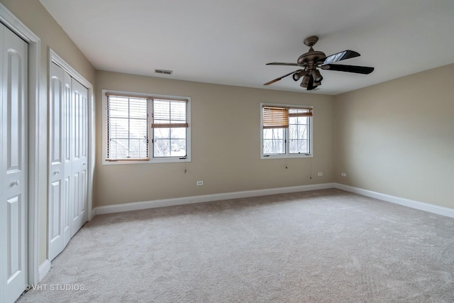 unfurnished bedroom featuring ceiling fan, light carpet, and two closets