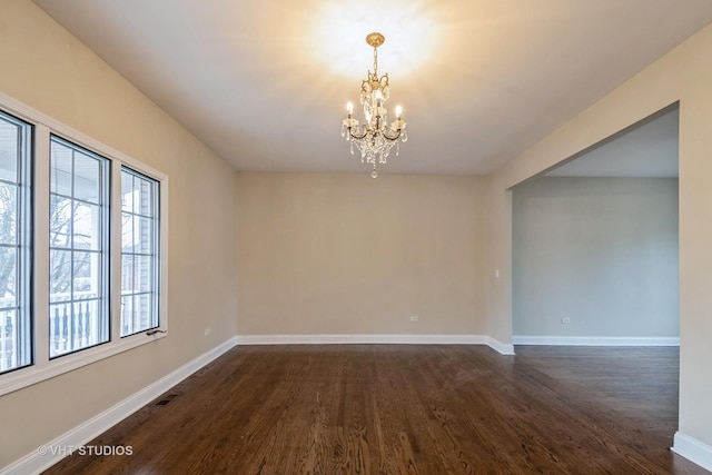 spare room featuring an inviting chandelier and dark wood-type flooring