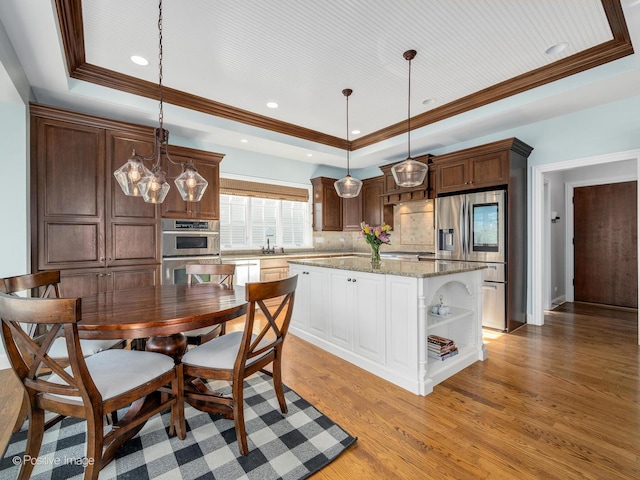 kitchen with decorative light fixtures, stainless steel appliances, a raised ceiling, and a kitchen island