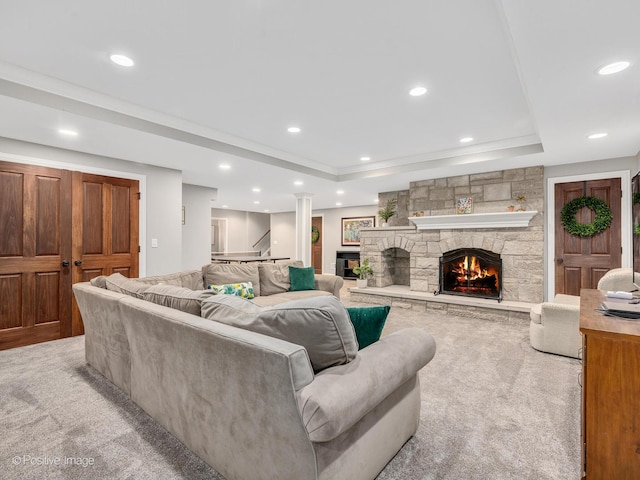 living room featuring light colored carpet, a stone fireplace, and a raised ceiling