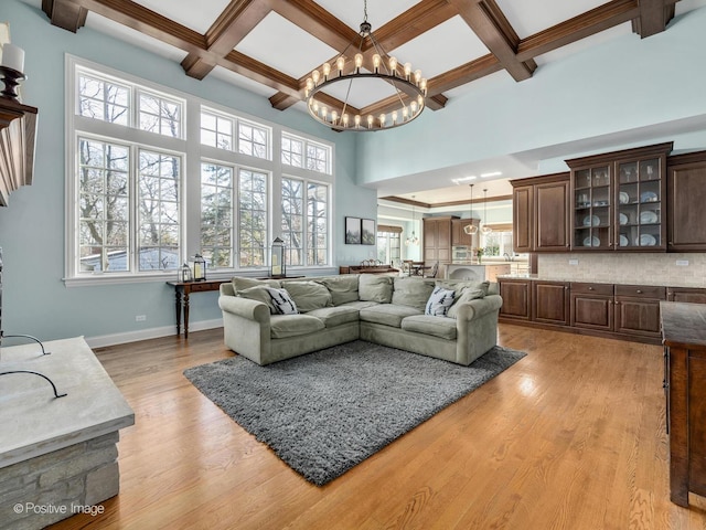 living room featuring coffered ceiling, a notable chandelier, a high ceiling, and light wood-type flooring