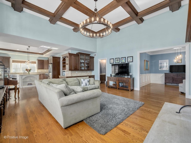 living room with beamed ceiling, wood-type flooring, ornamental molding, coffered ceiling, and a notable chandelier