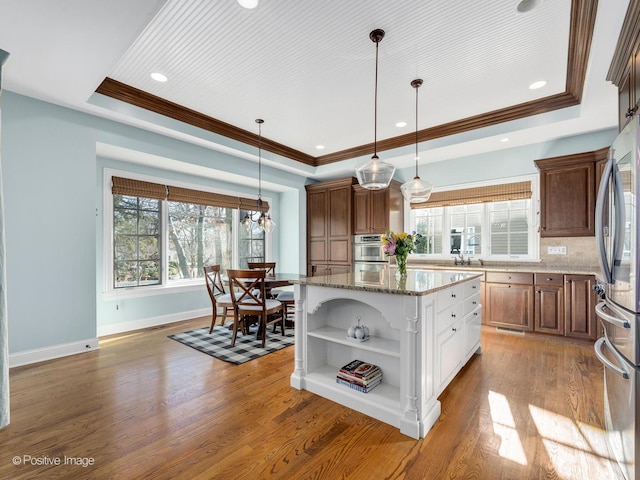 kitchen with wood-type flooring, appliances with stainless steel finishes, a tray ceiling, a kitchen island, and white cabinets