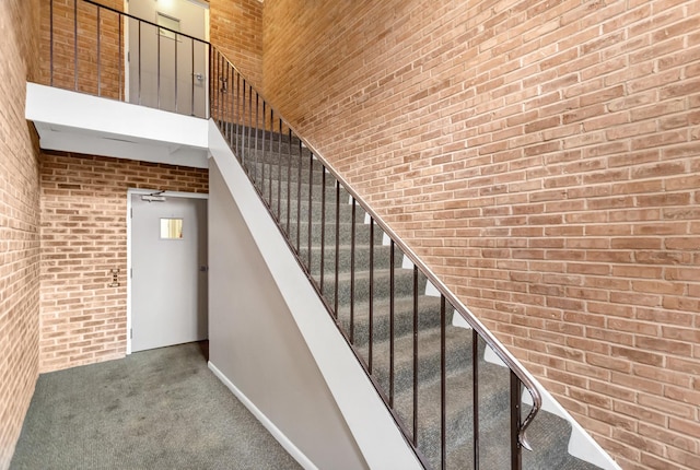 staircase featuring brick wall, carpet, and a towering ceiling