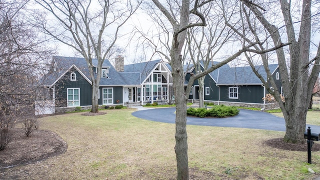 view of front of property with aphalt driveway, stone siding, a chimney, and a front lawn