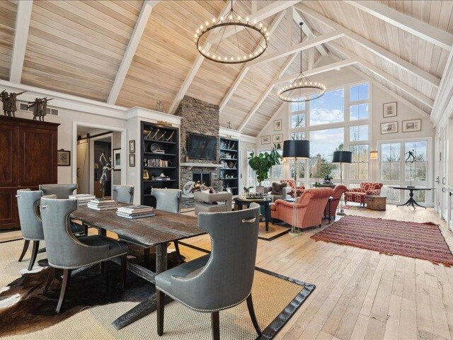 dining area featuring a fireplace, a notable chandelier, light wood-style flooring, wood ceiling, and high vaulted ceiling