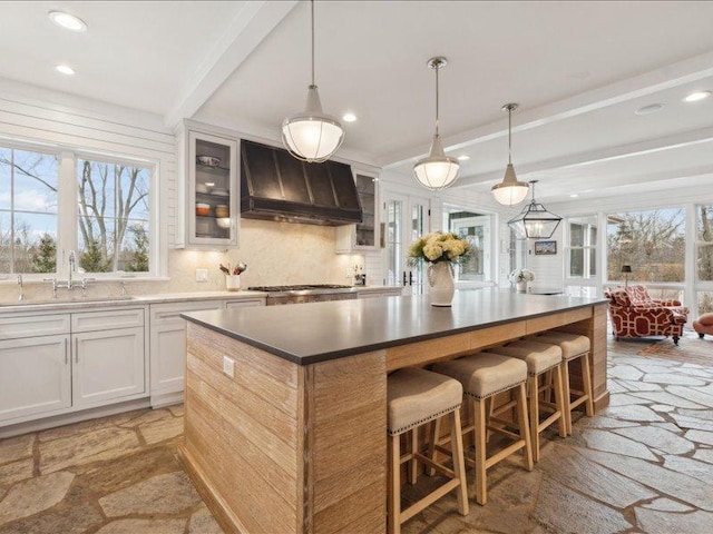 kitchen featuring tasteful backsplash, a kitchen island, beamed ceiling, custom exhaust hood, and stone tile flooring