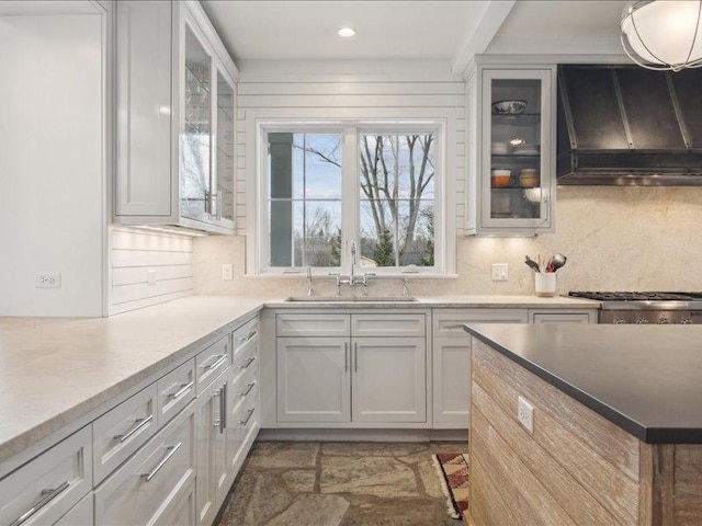 kitchen featuring a sink, backsplash, custom exhaust hood, and glass insert cabinets