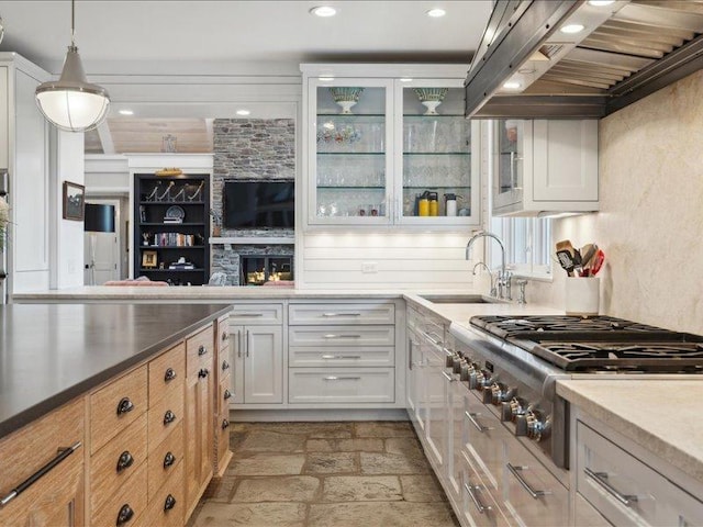 kitchen featuring stone tile floors, stainless steel gas cooktop, a sink, custom exhaust hood, and glass insert cabinets