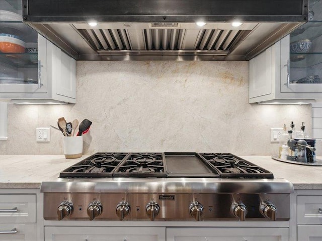 kitchen featuring stainless steel gas cooktop, premium range hood, white cabinets, backsplash, and glass insert cabinets