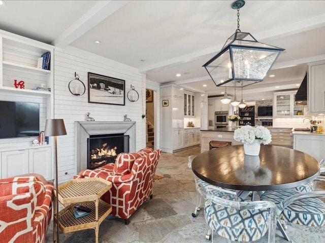 dining room with a lit fireplace, stone finish floor, beamed ceiling, and recessed lighting