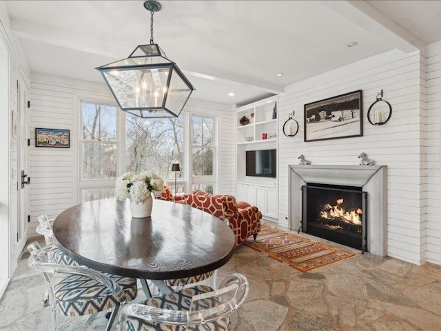 dining room featuring a lit fireplace, built in shelves, beamed ceiling, and wooden walls