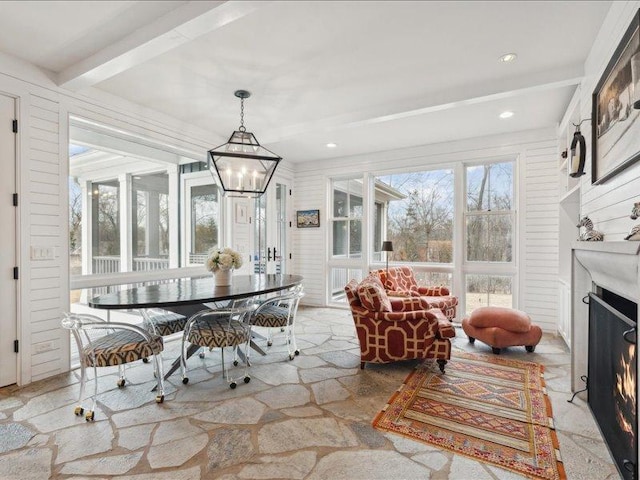 sunroom / solarium featuring a warm lit fireplace, a chandelier, and beam ceiling