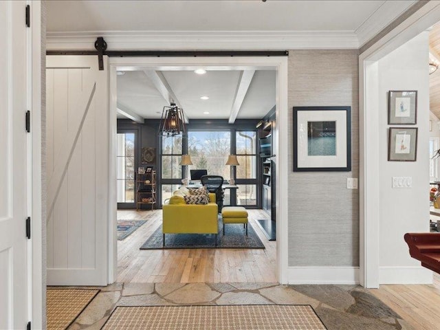 interior space featuring a barn door, baseboards, ornamental molding, hardwood / wood-style floors, and beamed ceiling