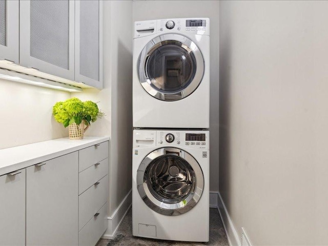 clothes washing area featuring stacked washing maching and dryer, cabinet space, and baseboards