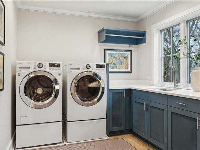 clothes washing area featuring ornamental molding, a sink, cabinet space, and washer and dryer