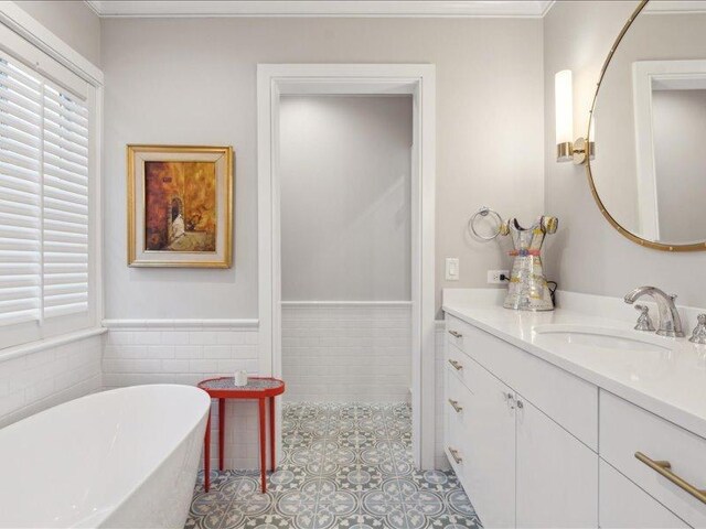 full bath with tile patterned flooring, vanity, tile walls, wainscoting, and a soaking tub