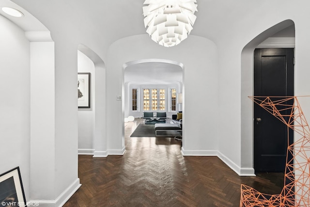 hall featuring an inviting chandelier, baseboards, and arched walkways