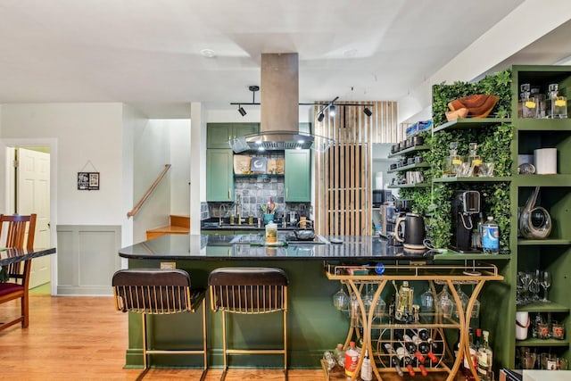 kitchen featuring a kitchen bar, black cooktop, green cabinetry, island range hood, and light wood-type flooring