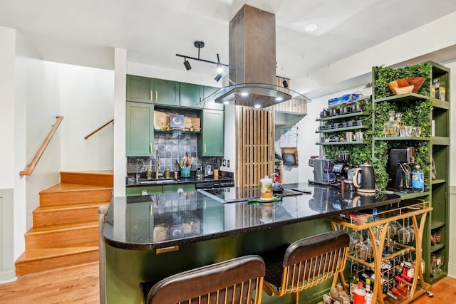 kitchen featuring sink, island range hood, light wood-type flooring, kitchen peninsula, and green cabinets