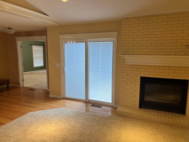 unfurnished living room with lofted ceiling, a brick fireplace, and light wood-type flooring