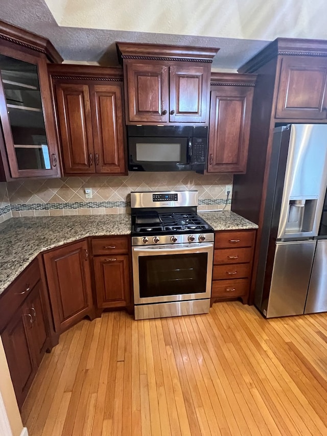 kitchen featuring light stone counters, a textured ceiling, light wood-type flooring, appliances with stainless steel finishes, and decorative backsplash