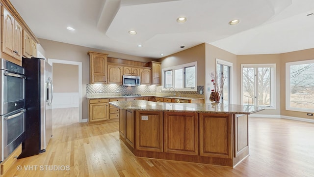 kitchen featuring sink, stone counters, stainless steel appliances, a kitchen island, and light wood-type flooring