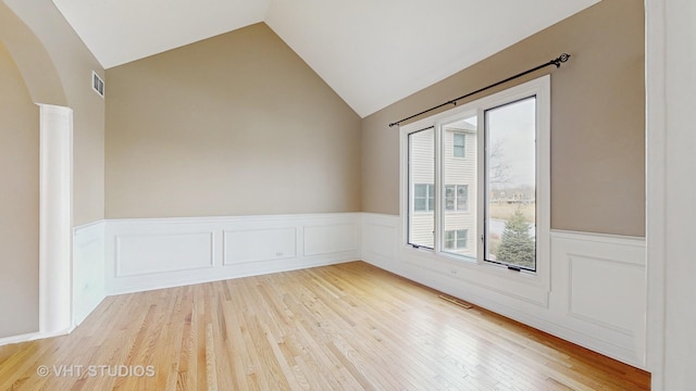 empty room featuring lofted ceiling, wood-type flooring, and ornate columns