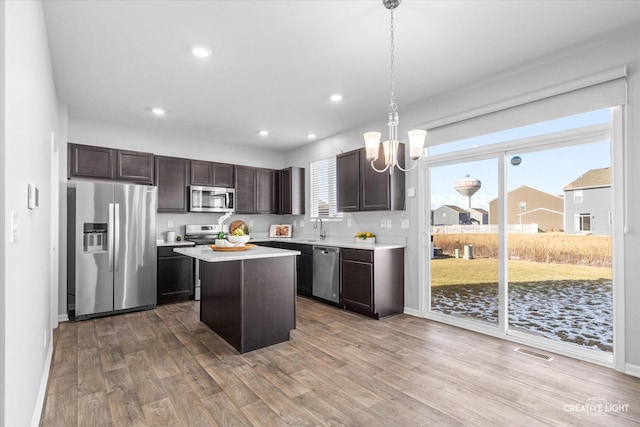 kitchen with sink, decorative light fixtures, appliances with stainless steel finishes, a kitchen island, and hardwood / wood-style floors