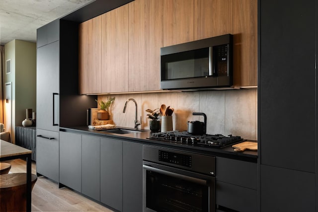 kitchen featuring gray cabinets, sink, stainless steel oven, black gas stovetop, and light wood-type flooring