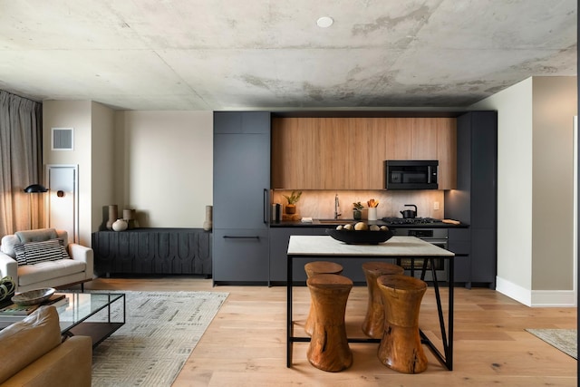 kitchen featuring decorative backsplash, light hardwood / wood-style floors, a kitchen breakfast bar, and appliances with stainless steel finishes