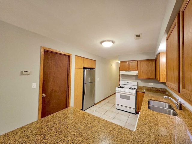 kitchen with white gas range, sink, light tile patterned floors, and stainless steel fridge