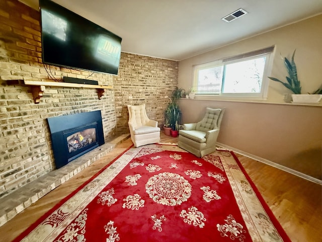 sitting room with hardwood / wood-style flooring, brick wall, and a brick fireplace