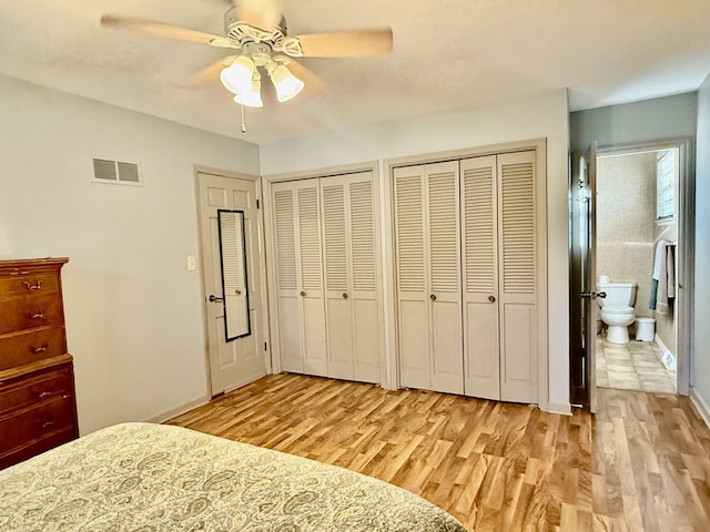 unfurnished bedroom featuring ceiling fan, light hardwood / wood-style floors, ensuite bath, and two closets