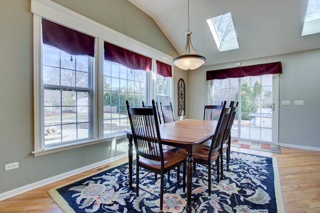 dining space featuring lofted ceiling with skylight, baseboards, and wood finished floors